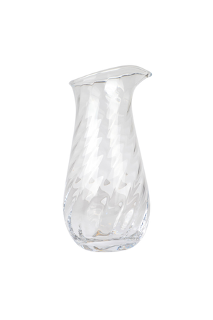 Mundblæst kande i klart glas med svagt skråt hældetud og organisk form. Overfladen er dekoreret med et snoet, optisk mønster, der skaber en elegant struktur i glasset.