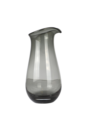 En enkel, mundblæst glaskande i røgfarvet glas. Kanden har en blød, rund form med smal hals og hældetud. Designet er minimalistisk uden mønster, og glasset er let gennemsigtigt med en gråtonet finish.