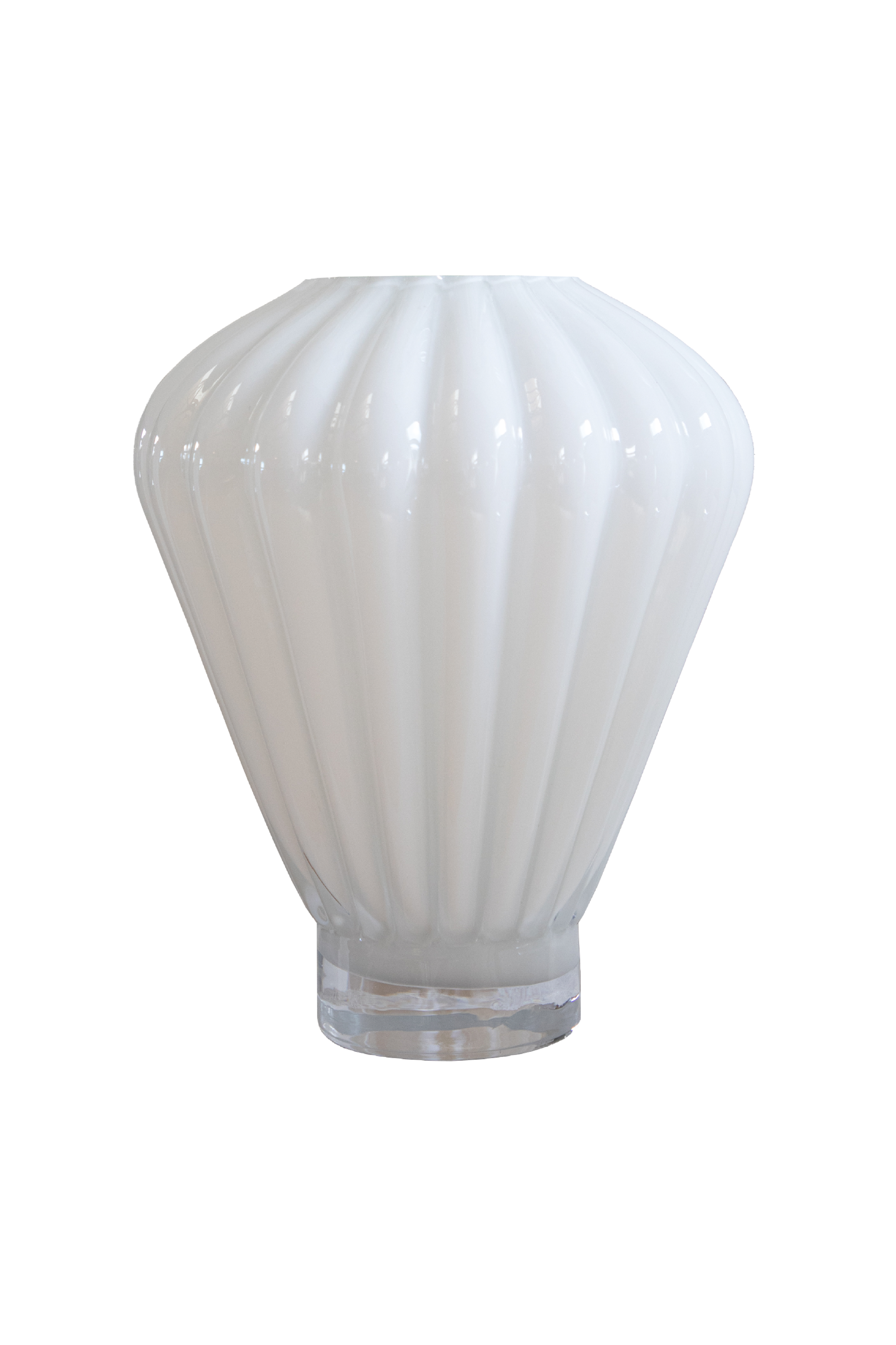 En hvid, opalglas vase med lodrette riflede linjer og en rund, bred form, der smalner ind mod bunden. Vasen står på en gennemsigtig glasfod. Baggrunden er hvid og neutral.