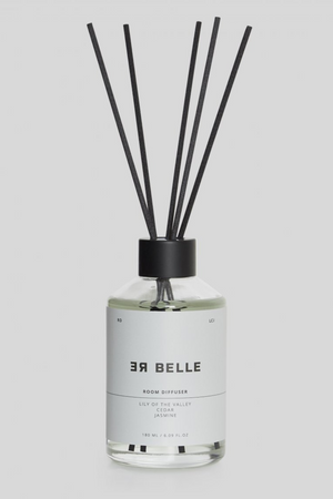En gennemsigtig glasflaske med sort låg og flere sorte duftpinde. Etiket i hvidt med sort tekst: “ER BELLE ROOM DIFFUSER, LILY OF THE VALLEY, CEDAR, JASMINE, 180 ML