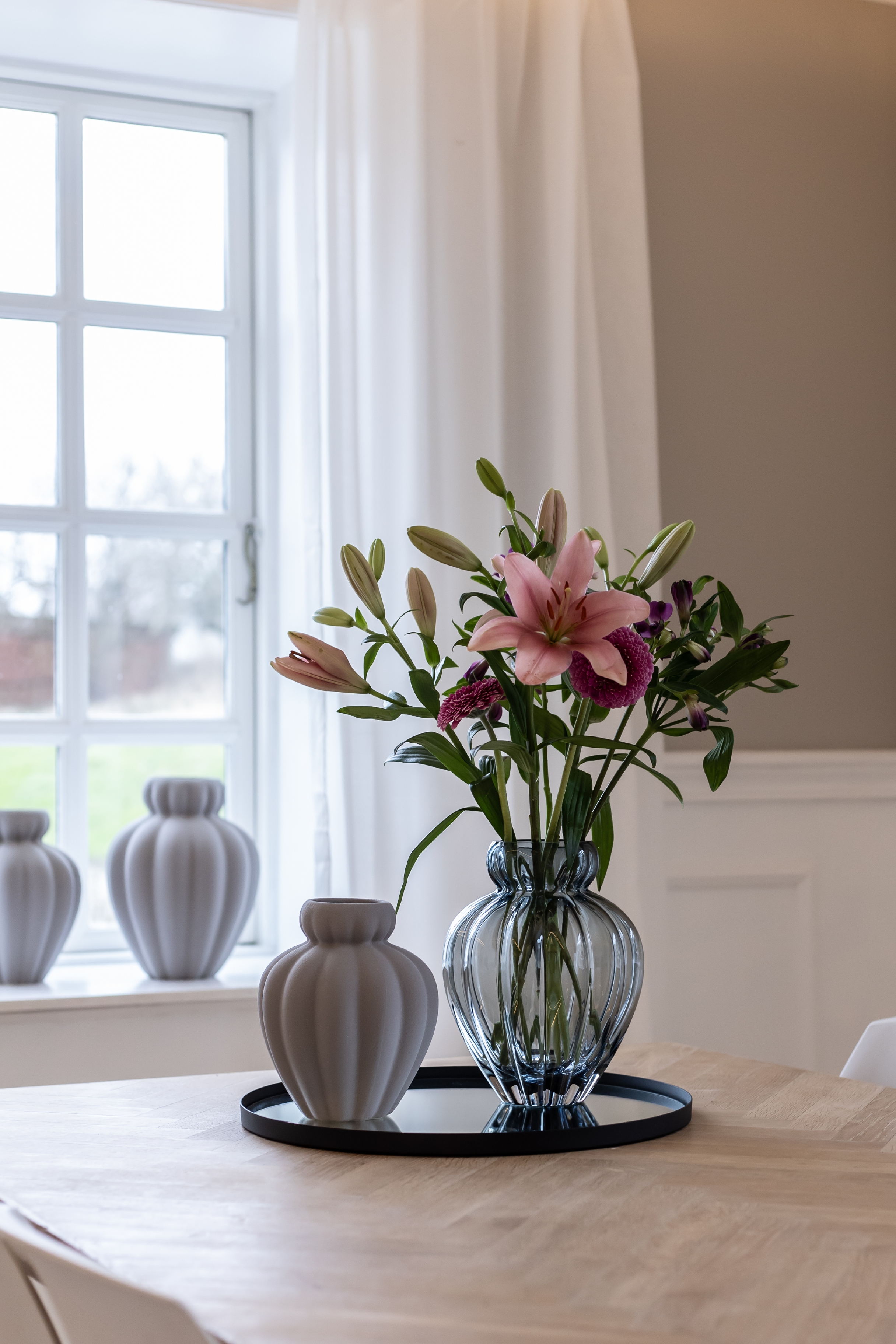 Rund spejlbakke i grå, stylet på et spisebord med vaser fra Specktrum.