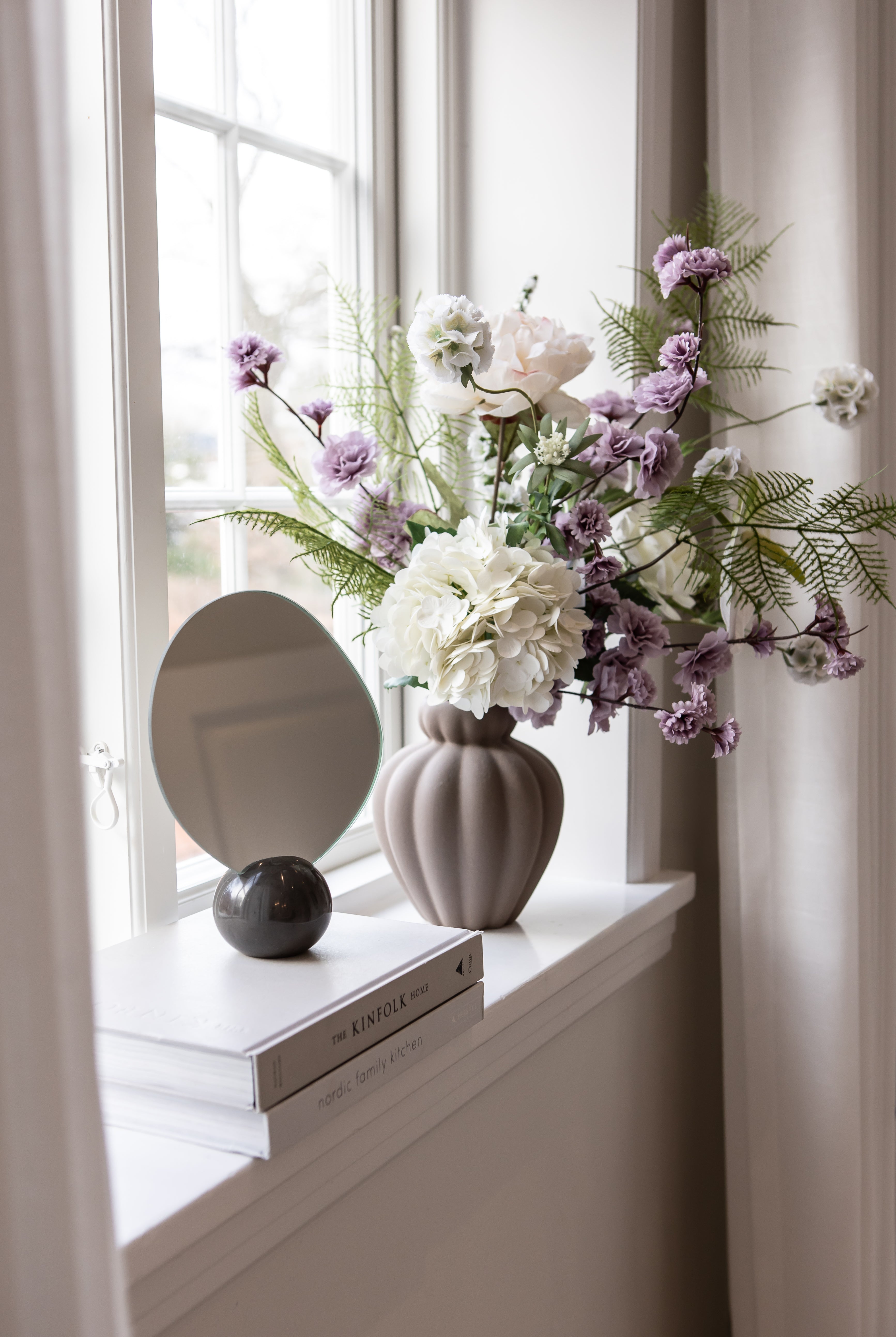 Asta bordspejlet med marmorfod i farven lightning stylet i en vindueskarm sammen med en vase med buket.