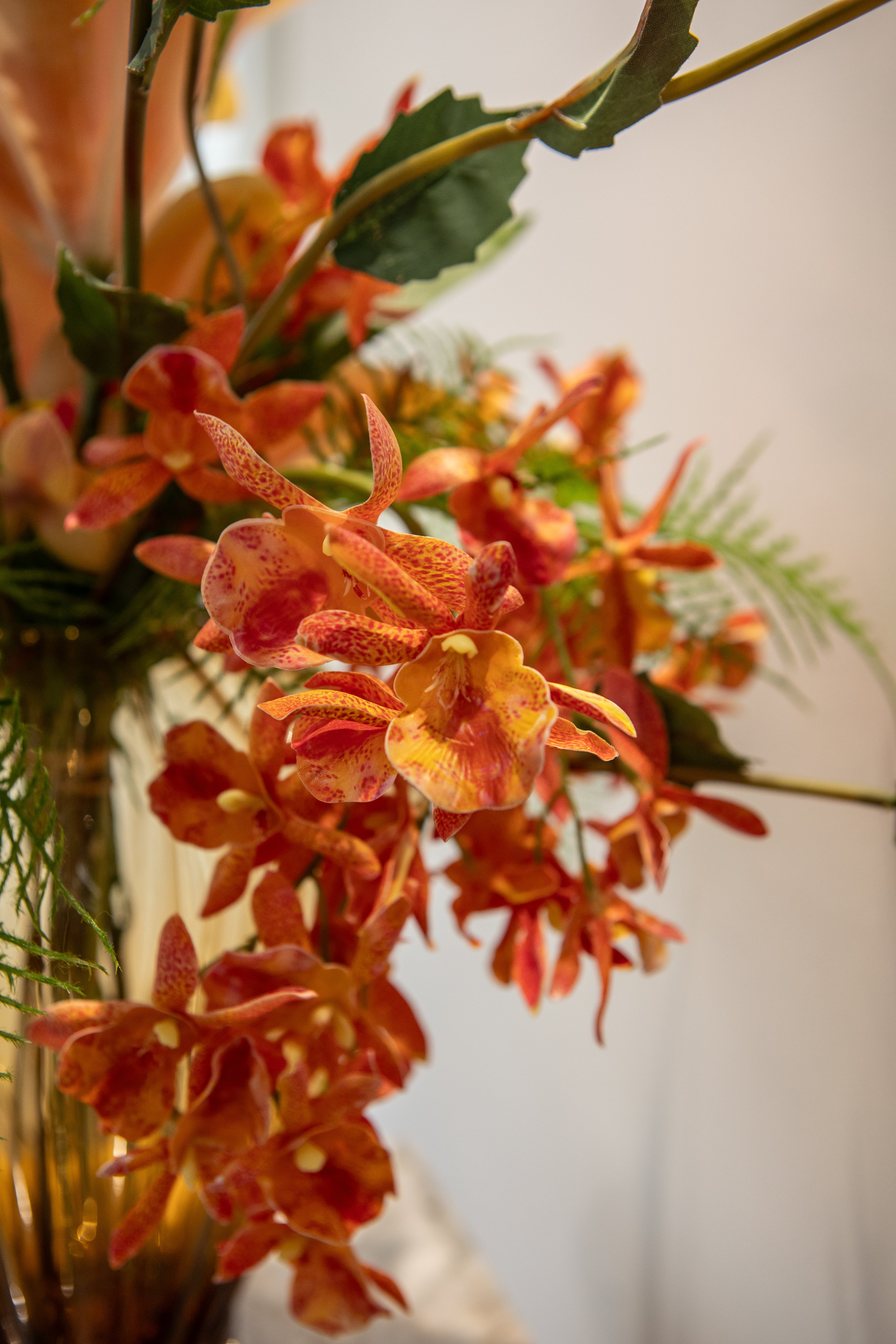 Nærbillede af en flerhovedet orange orkidé i en buket og en amber farvet glasvase.