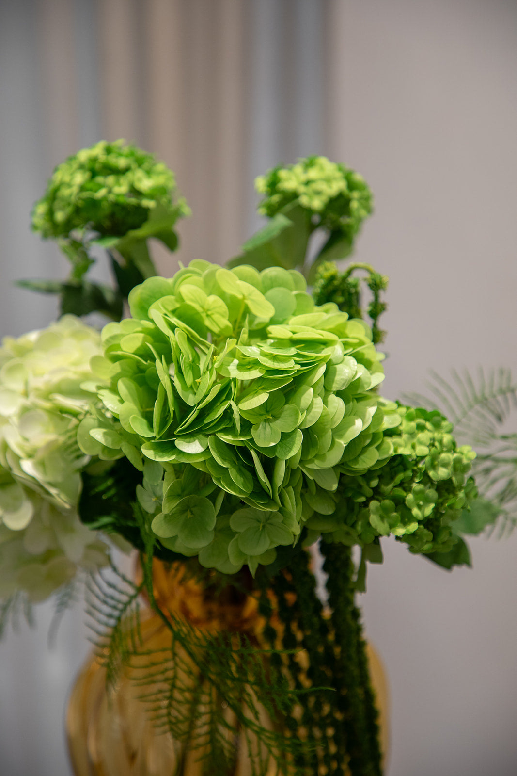 Nærbillede af buket af kunstige blomster i grønne nuancer. Placeret i en orange farvede glasvase.