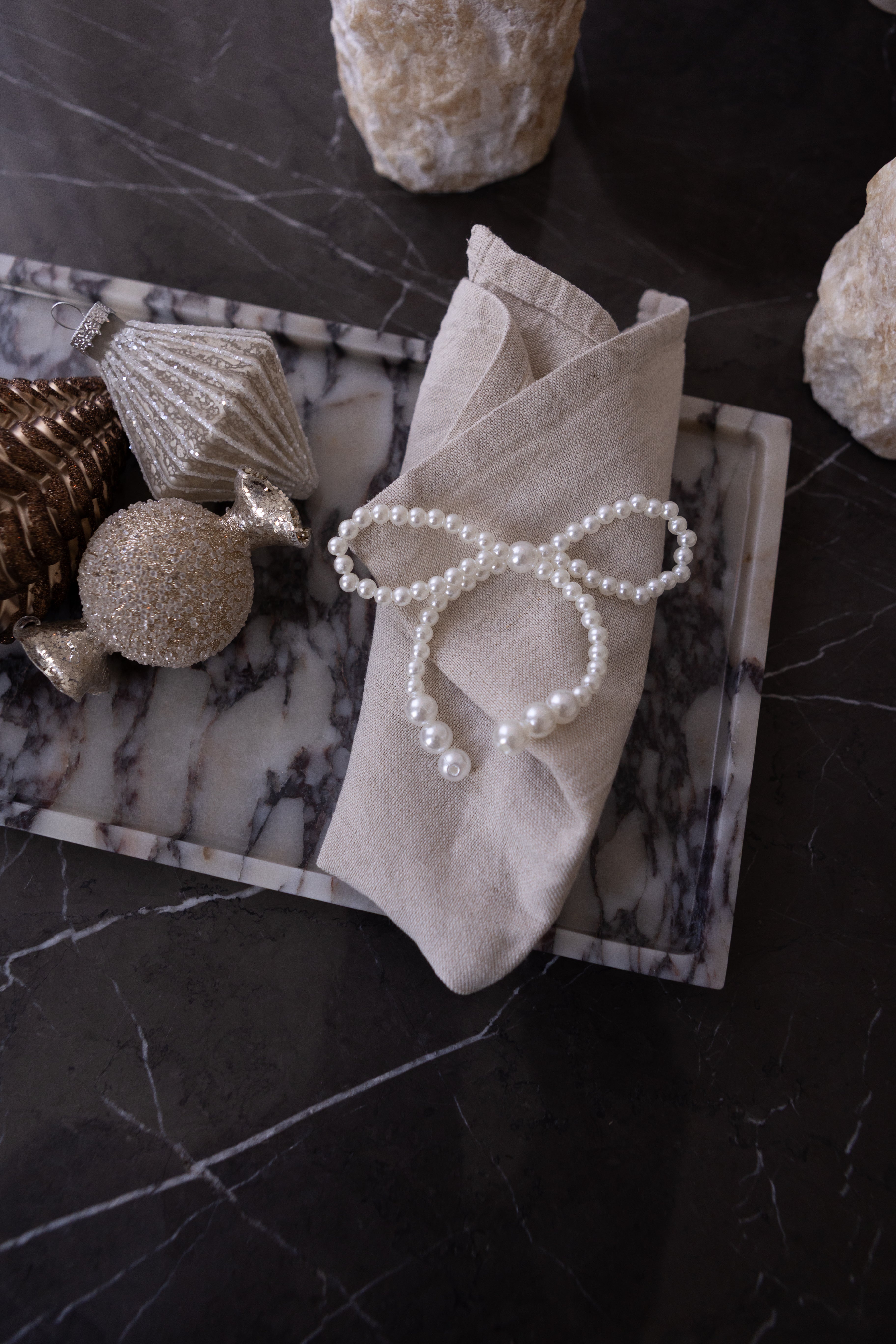 Sløjfe med perler, der ligger på en serviet ovenpå en marmorbakke. Ved siden af ligger tre julekugler.