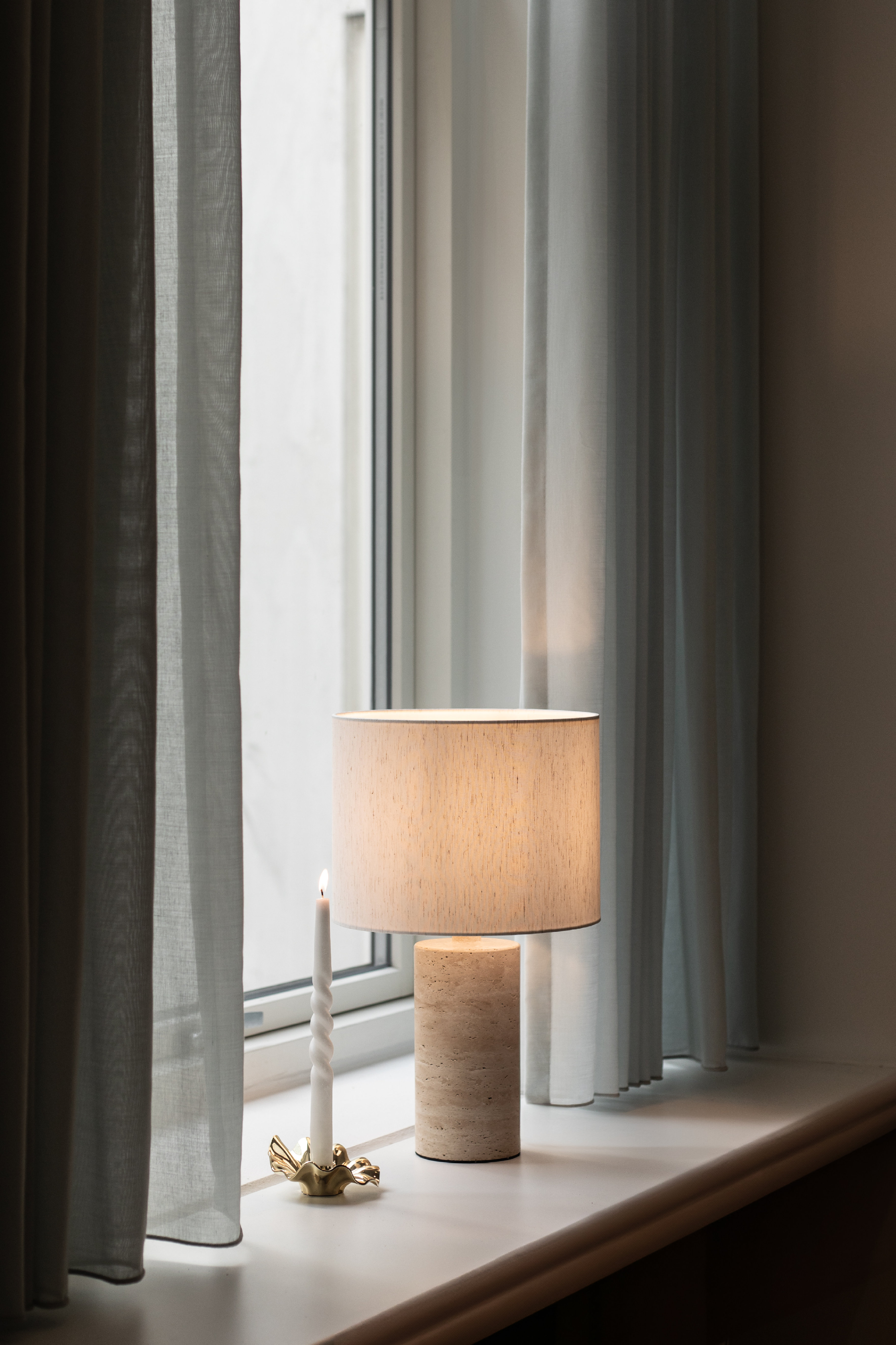 Sylvester lampskærm i hvid stylet med en marmor lampefod og en metal lysestage i vindueskarmen.