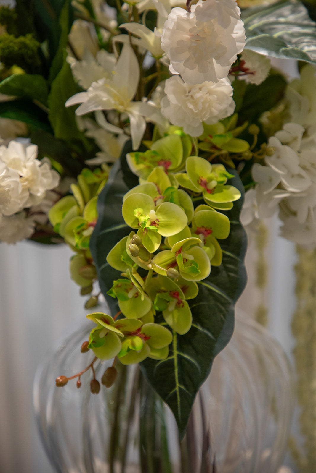 Nærbillede af kunstig buket i grønne og hvide nuancer, placeret i en gennemsigtig glasvase