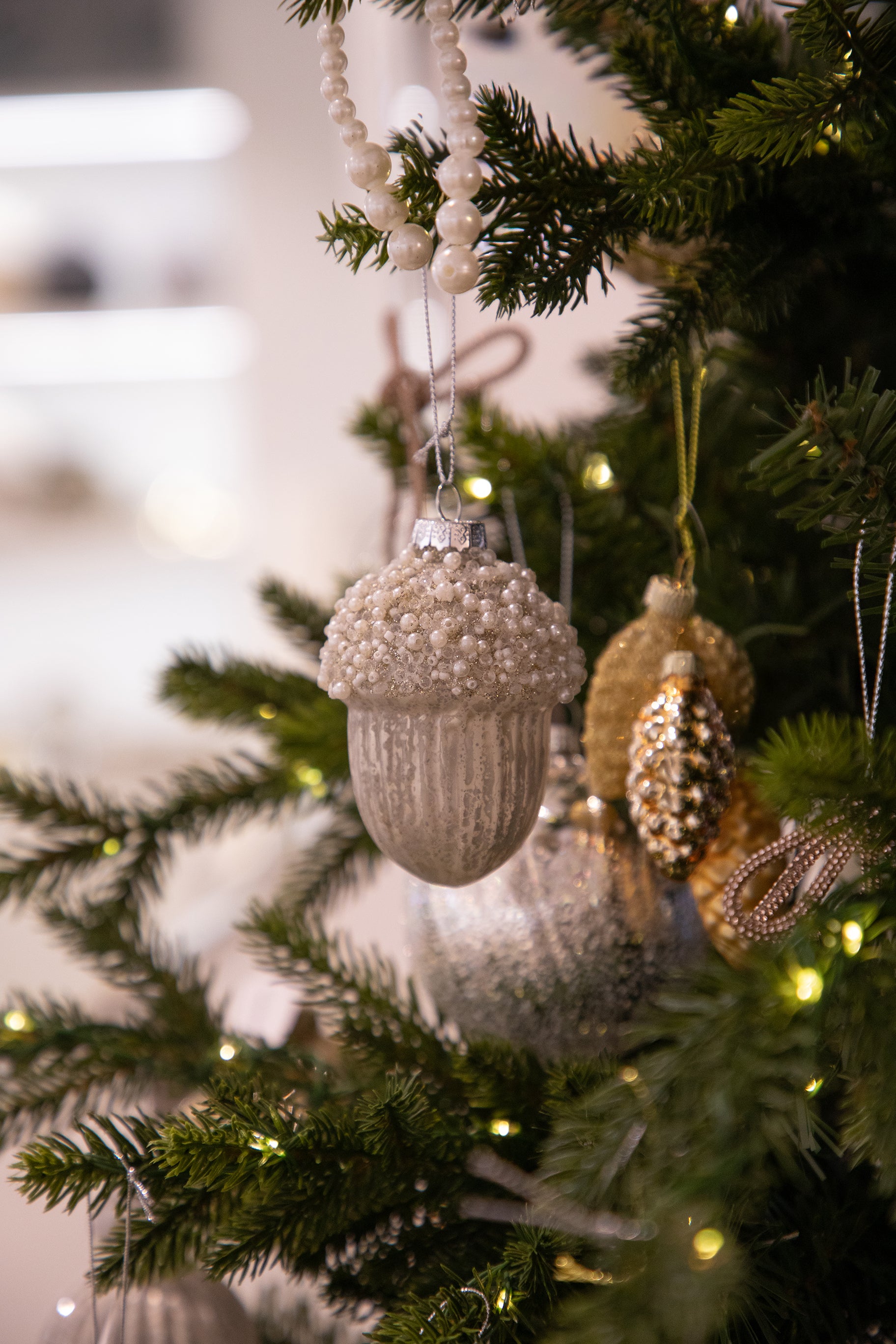 Agern julekugle i sølv med perle detaljer, der hænger på et juletræ.