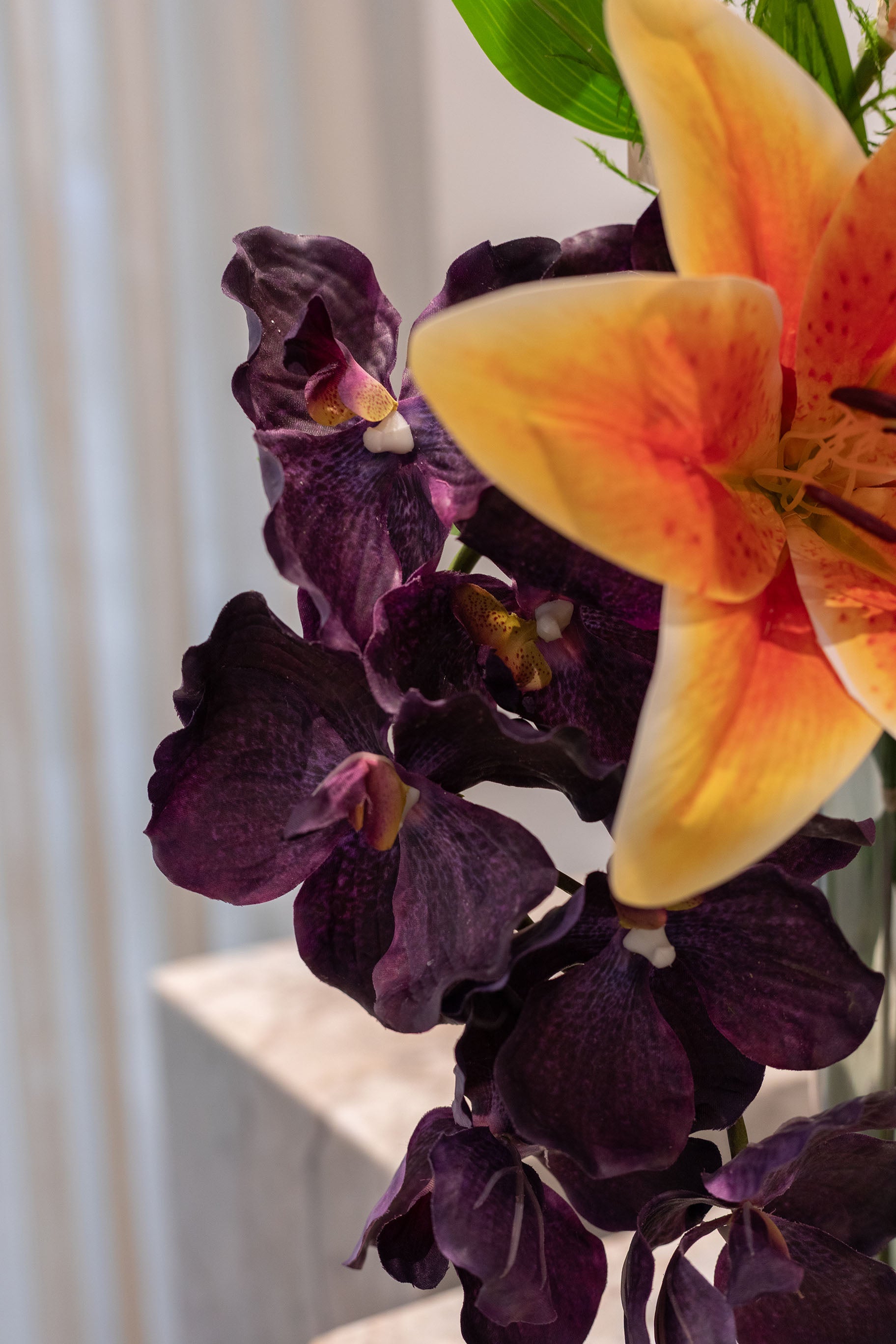 Nærbillede af flerhovedet mørke lilla orkidé. En del af en buket af kunstige blomster i orange og grønne nuancer.