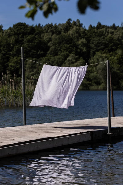 Video af Chloe Sengetøj i farven lavendel, der hænger på en tørresnor på en badebro ved vandet.