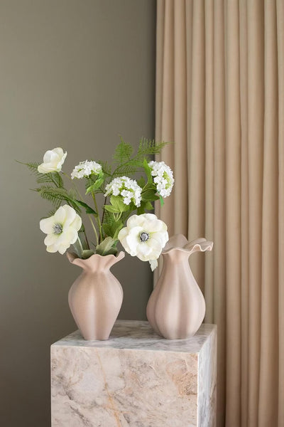 To keramikvaser i hver sin størrelse i en sand farve, med en lille kunstig buket i hvid og grøn i den mindste af vaserne. Vaserne er placeret på en marmor pedestal.