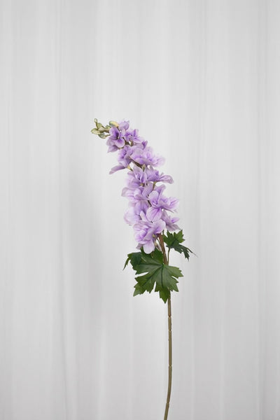 Video af Kunstig consolida blomst i en lyselilla farve med grønne blade i bunden. 