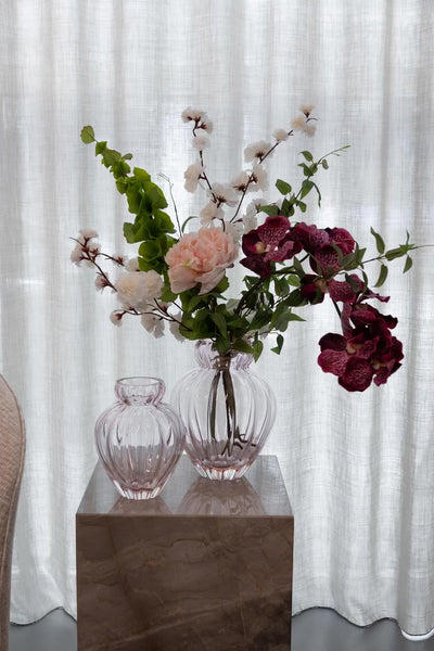 Video af en buket i en lyserødvase, der står ovenpå en marmor pedestal foran et hvidt gardin.