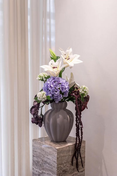 Video af grå penelope vase, med en buket i lilla og hvide nuancer, står på en pedestal.