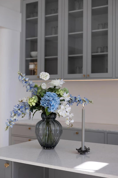 Video af Audrey vase i blå, med en buket i blå, grønne og hvide nuancer. Står på et køkkenbord med en lysestage og levende lys ved siden af.