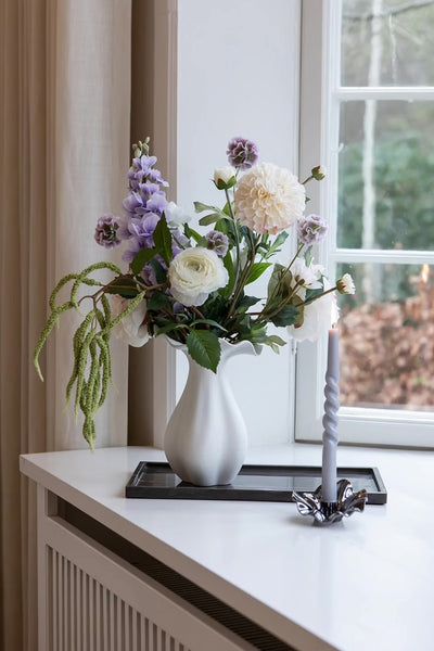 Kunstig buket i en vid keramik vase placeret på en spejlbakke.