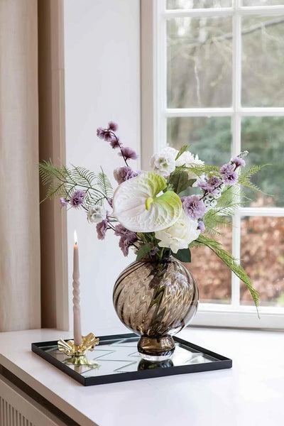 Video af herringbone spejl bakke i kvadratisk, der står i en vindueskarm. På bakken står en glasvase med kunstige blomster og en lysestage med et snoede lys.