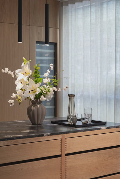 Penelope vasen i mellem i farven brun, stylet på en køkkenø med en stor buket. 