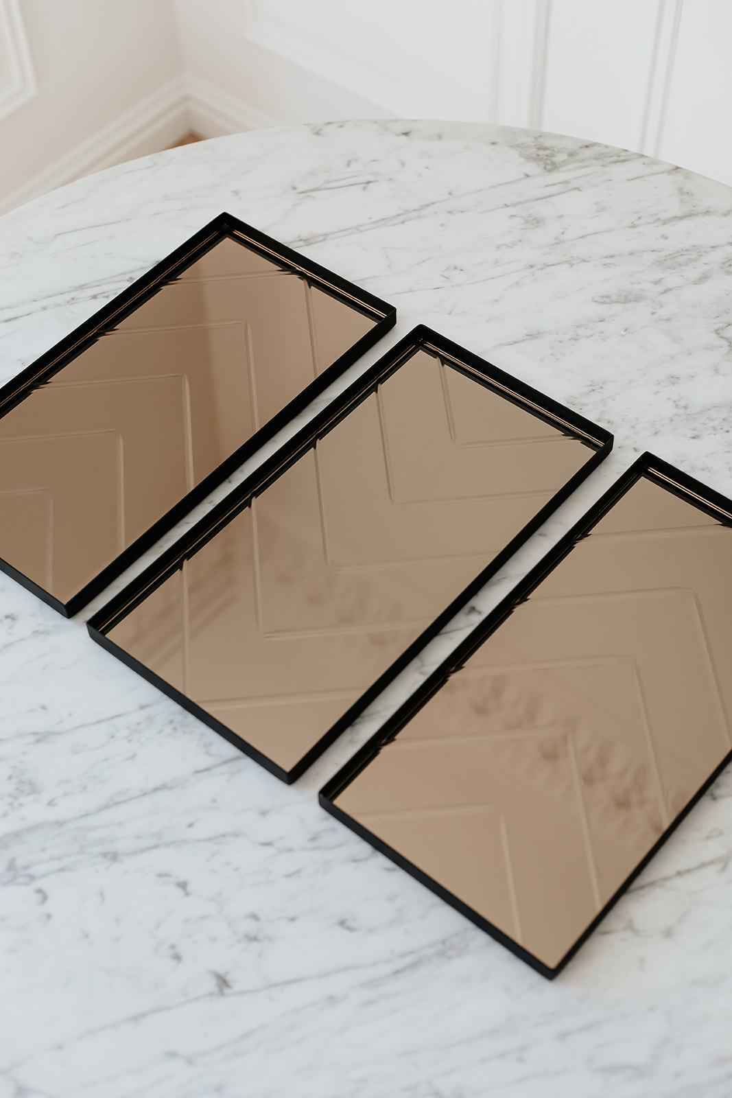 Tre rektangulære bakker med bronzefarvet spejloverflade ligger ved siden af hinanden på et rundt marmorbord.